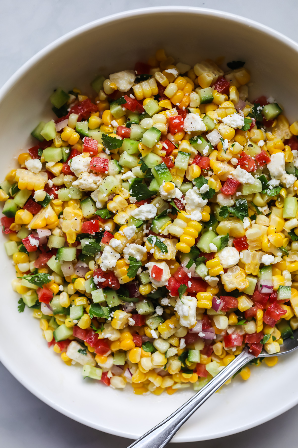 Corn salad in white bowl with spoon.